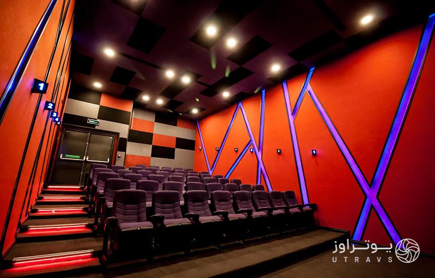 یک سالن سینما در برج آرمیتاژ مشهد که پنج ردیف صندلی دارد و دیواری قرمزرنگ با نورهای مخطط آبی.
